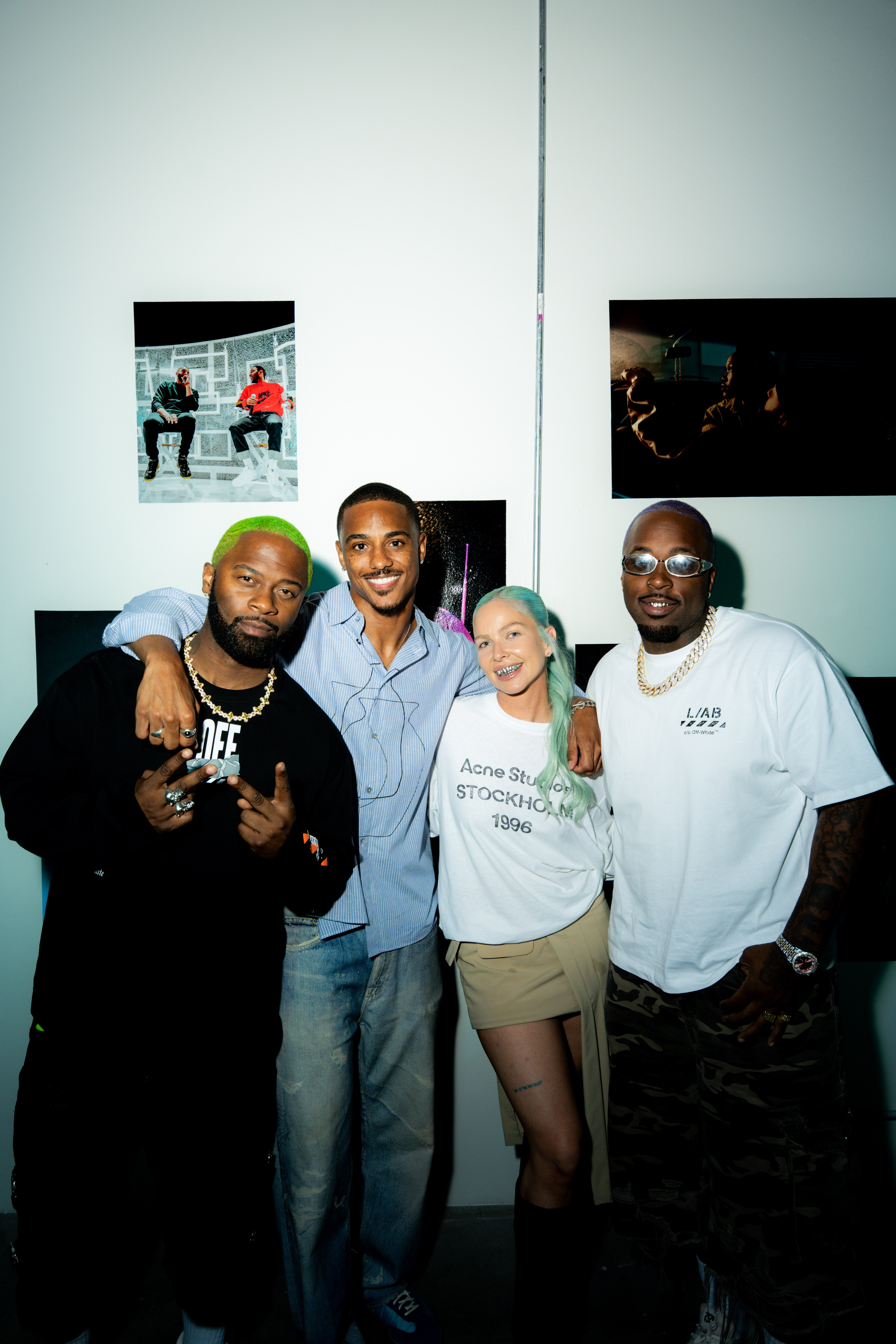  - Four people pose together in front of photographs displayed on gallery wall