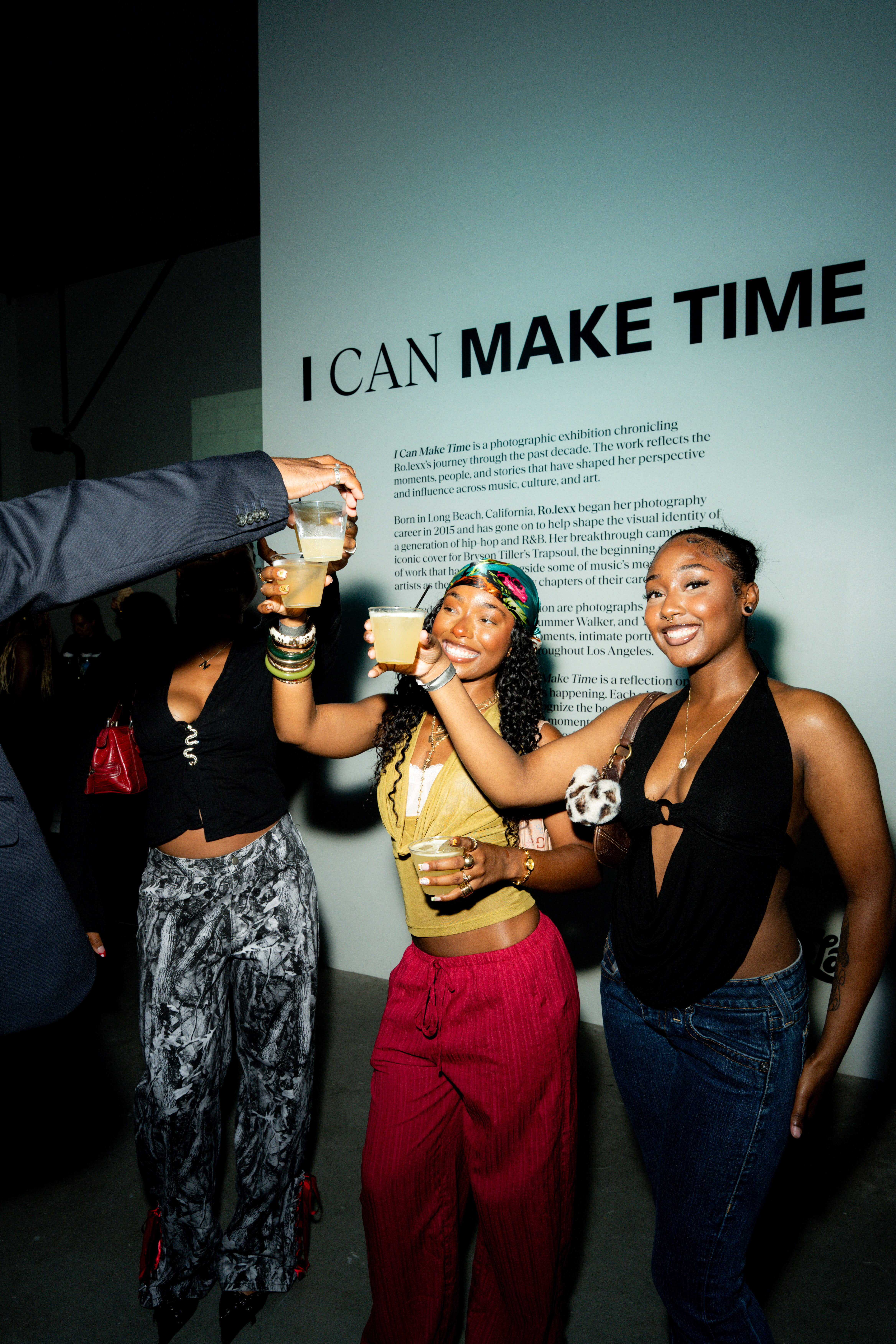 Three people raise drinks together in front of I Can Make Time exhibition statement