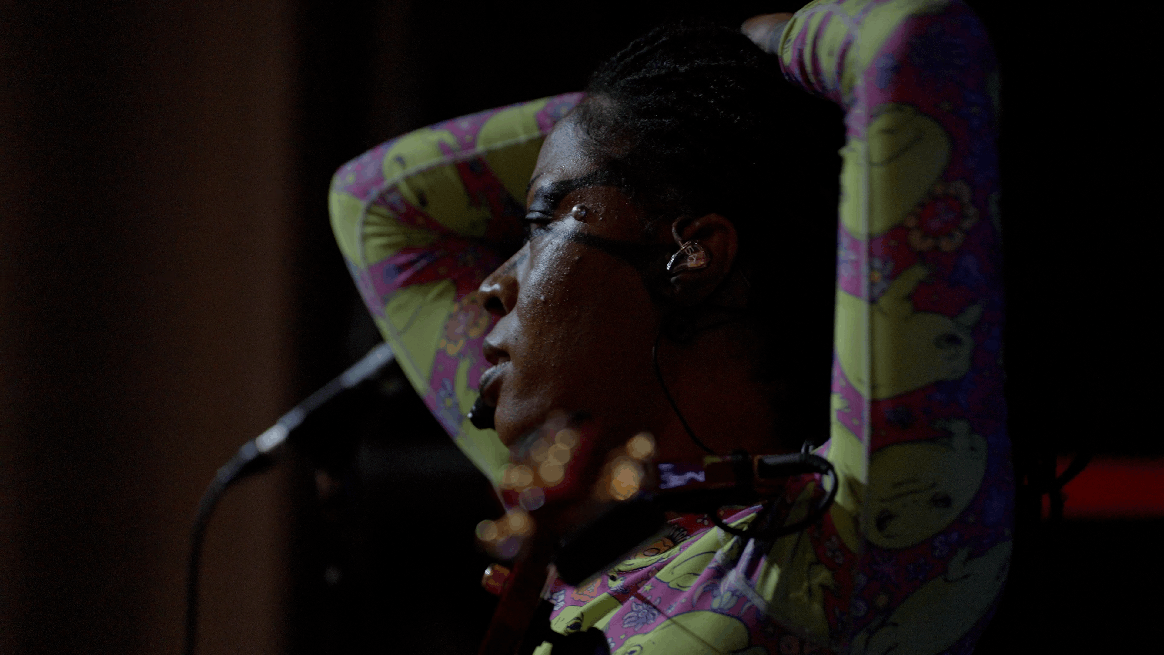 Performer wearing headset microphone rests arms behind their head onstage