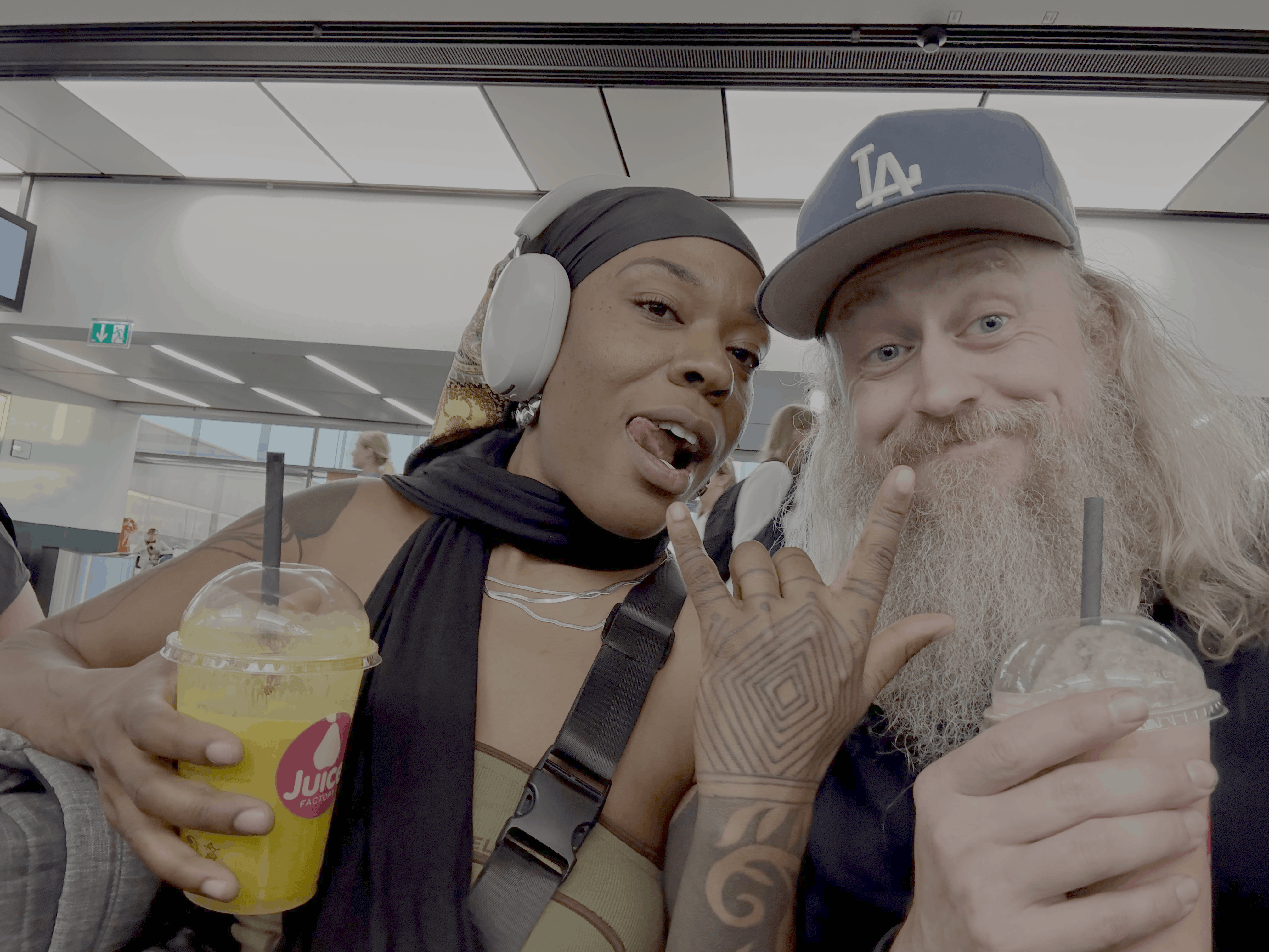 Two people pose for a selfie holding drinks and making hand gestures