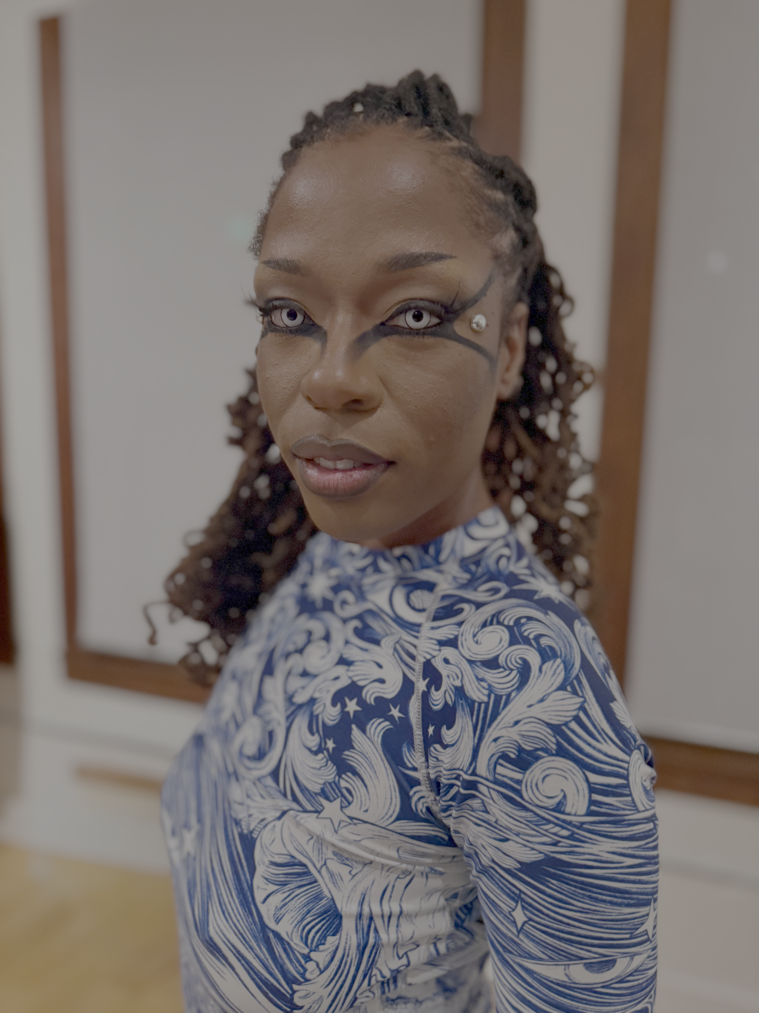 Performer with graphic eye makeup poses in blue and white patterned top