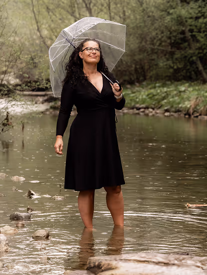 Nadine Wienecke von Gesund-Zeit Holistic Health steht in einem Fluss mit einem Regenschirm