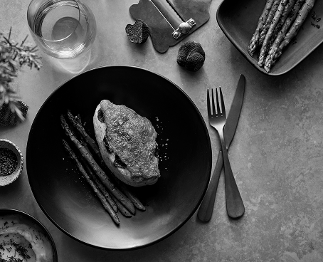 Plate with cooked asparagus and bread with spread, fork and knife beside, and a glass of water on table.
