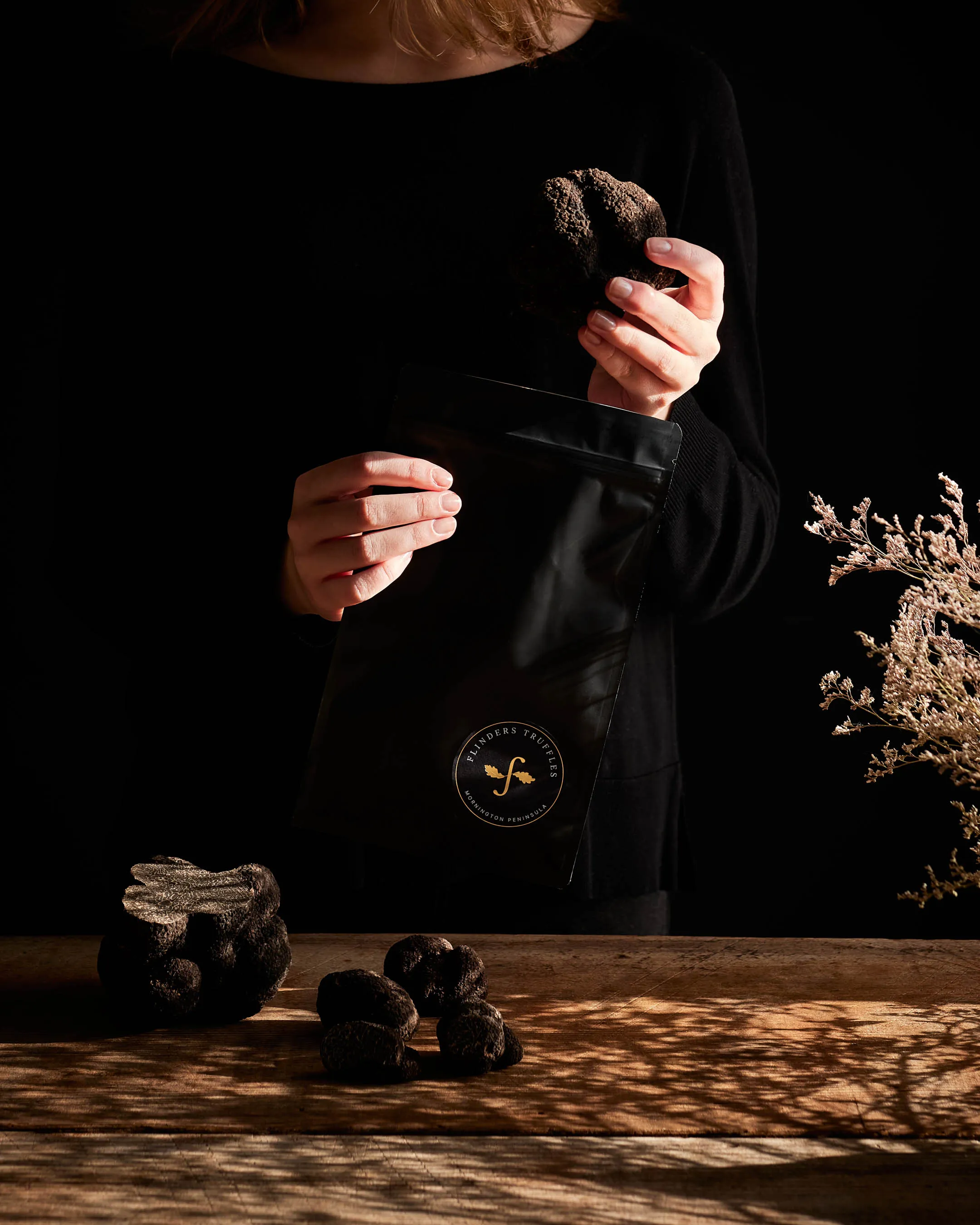 Person holding a large black truffle and a black resealable bag with Flinders Truffles logo.