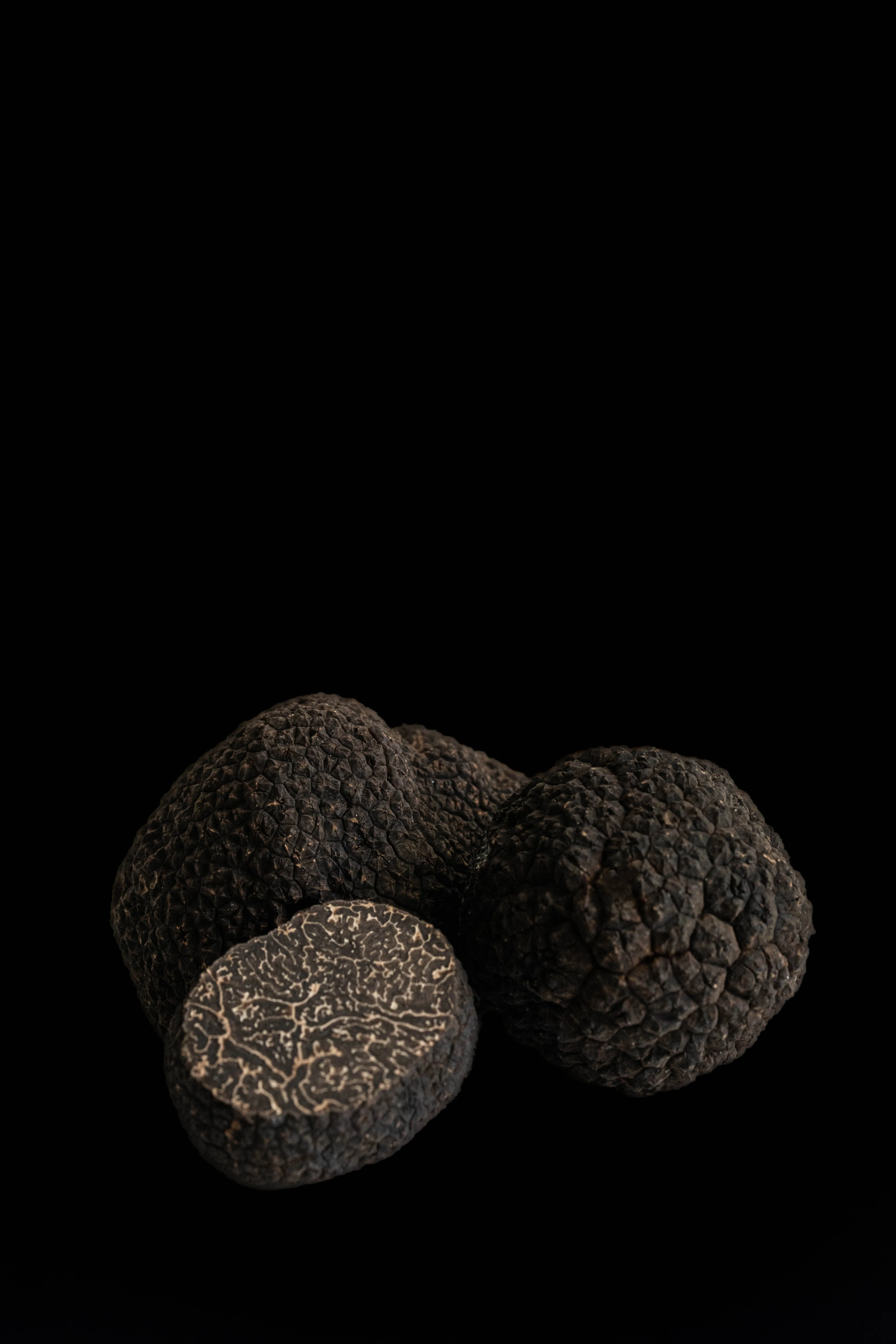 Close-up of whole and sliced black truffles on a black background.