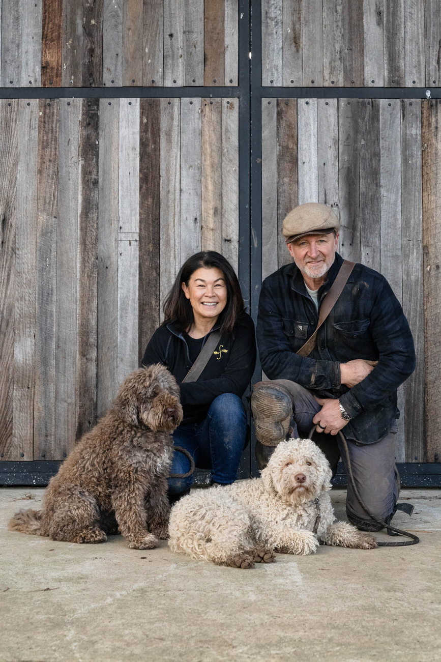 Flinders Truffles with two curly-haired truffle dogs in front of rustic wooden doors.