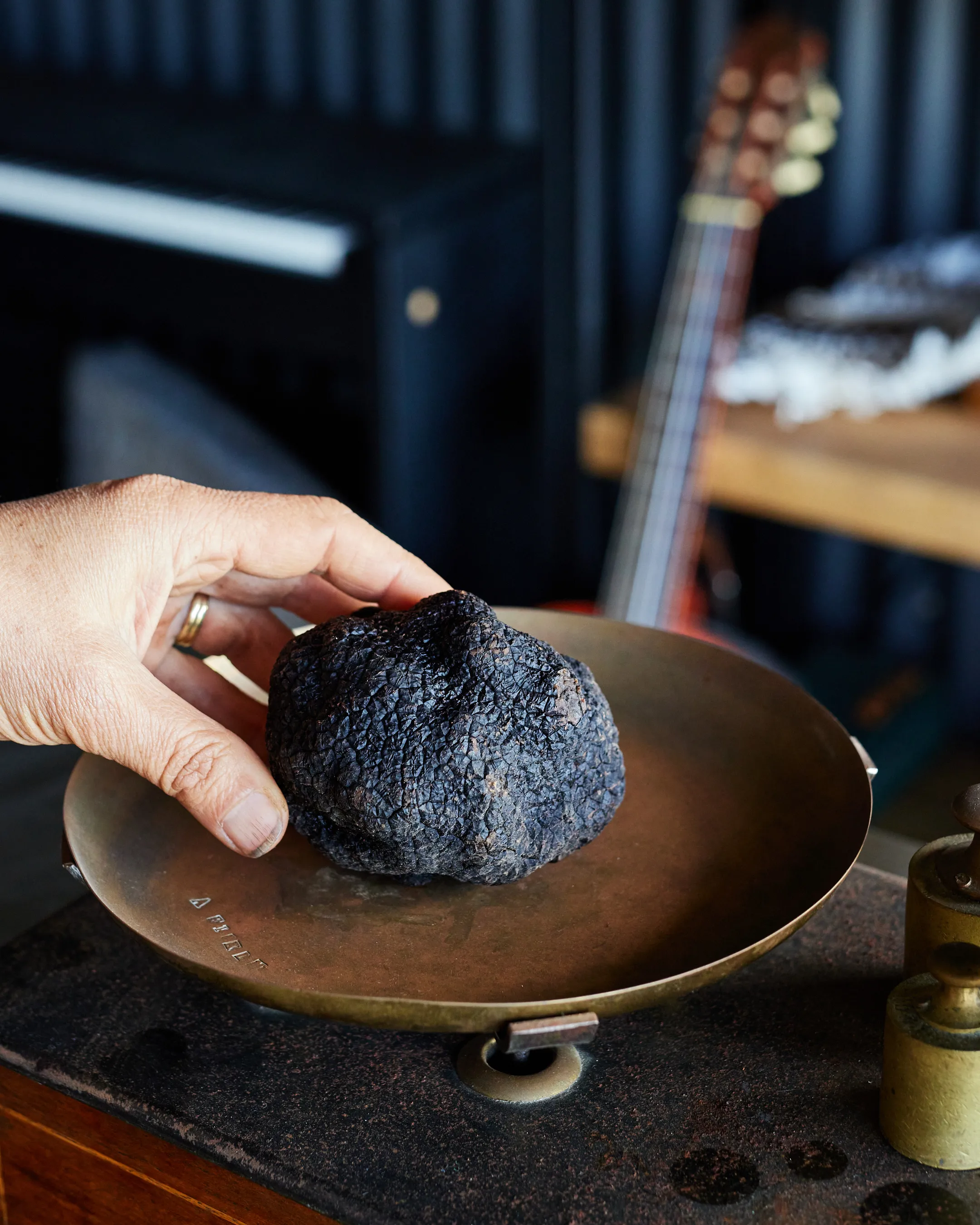 Hand holding a large black truffle on a vintage brass scale.