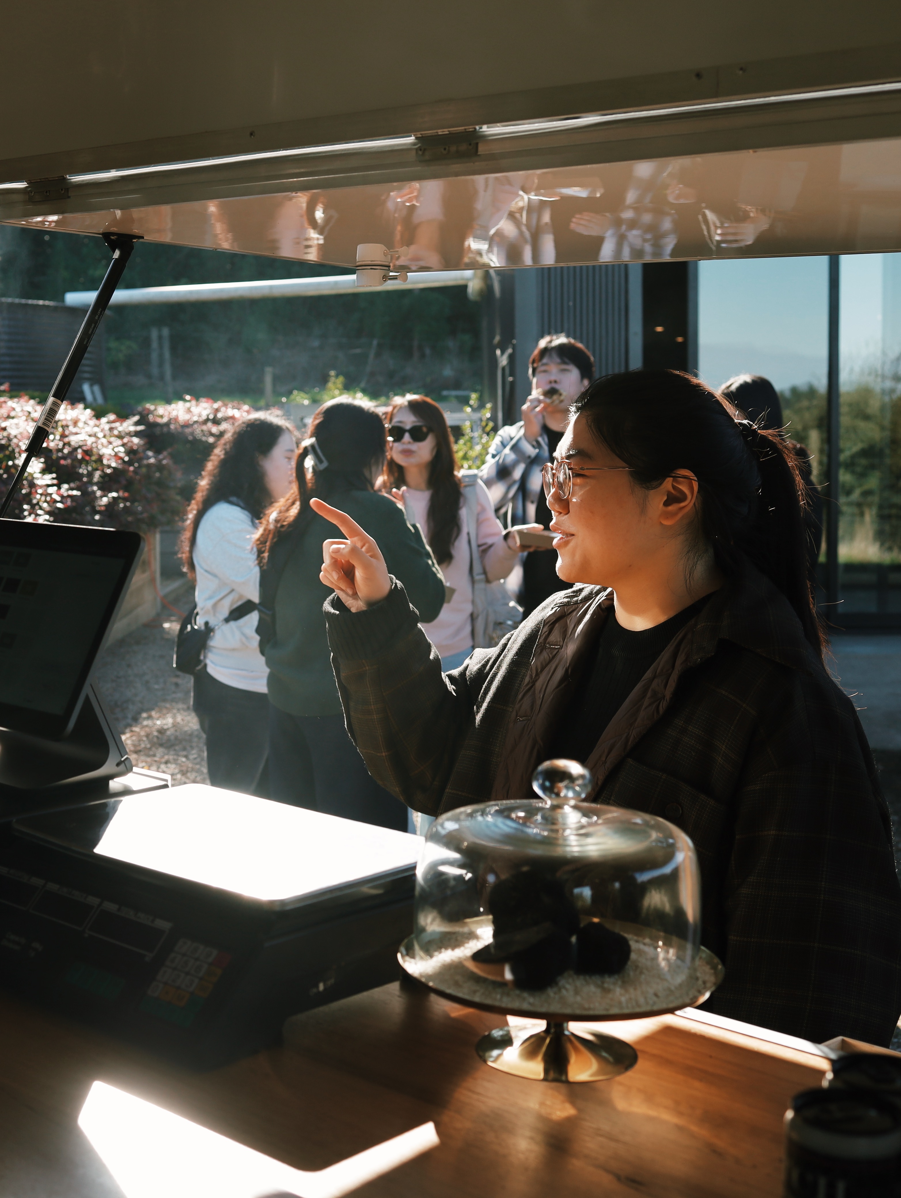 Woman in glasses pointing and ordering at the Flinders Truffles Van with a glass-covered plate of pastries, with people in the background.