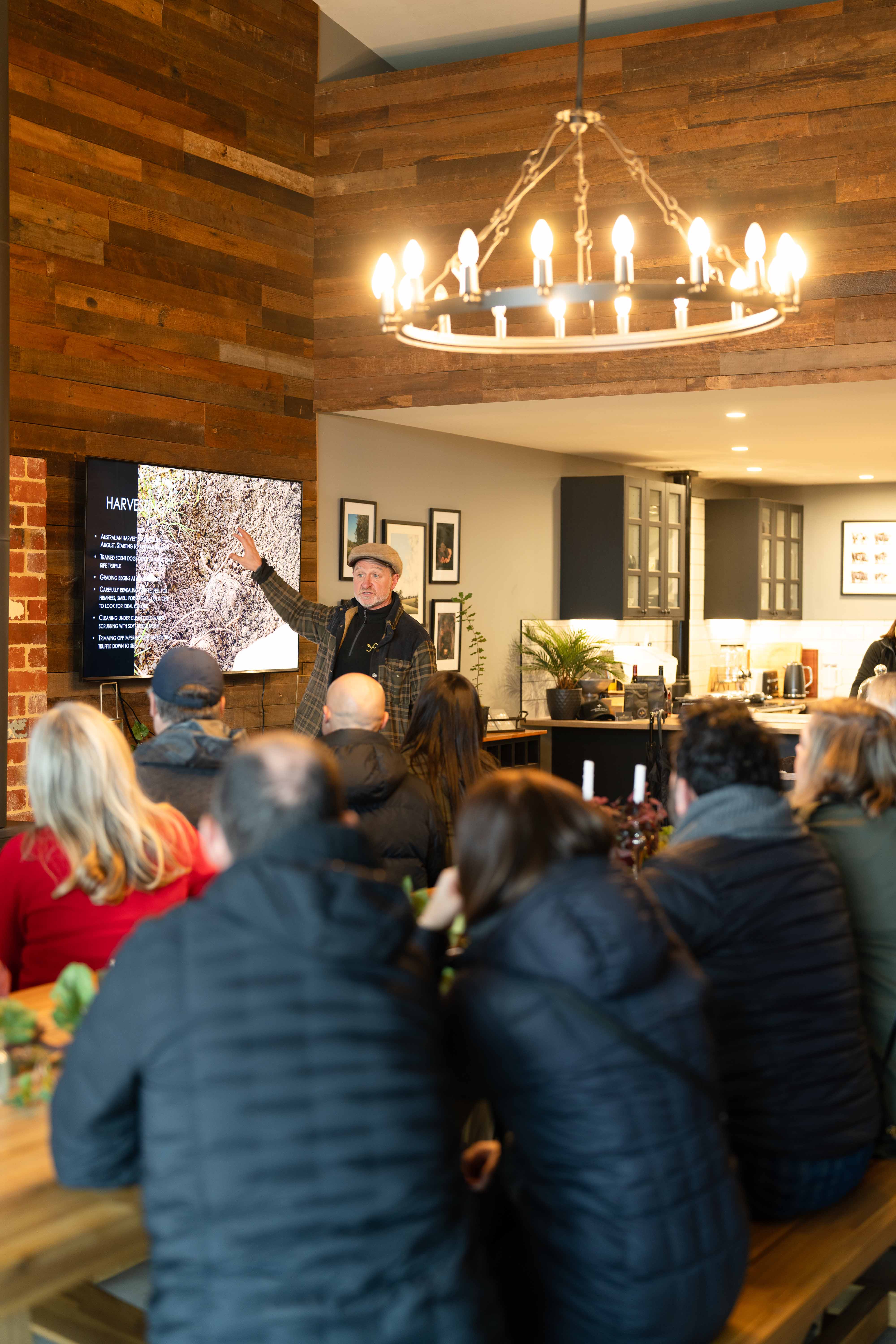 Flinders Truffles Venue. A presentation to seated audience in a cozy room with wood walls and a chandelier.