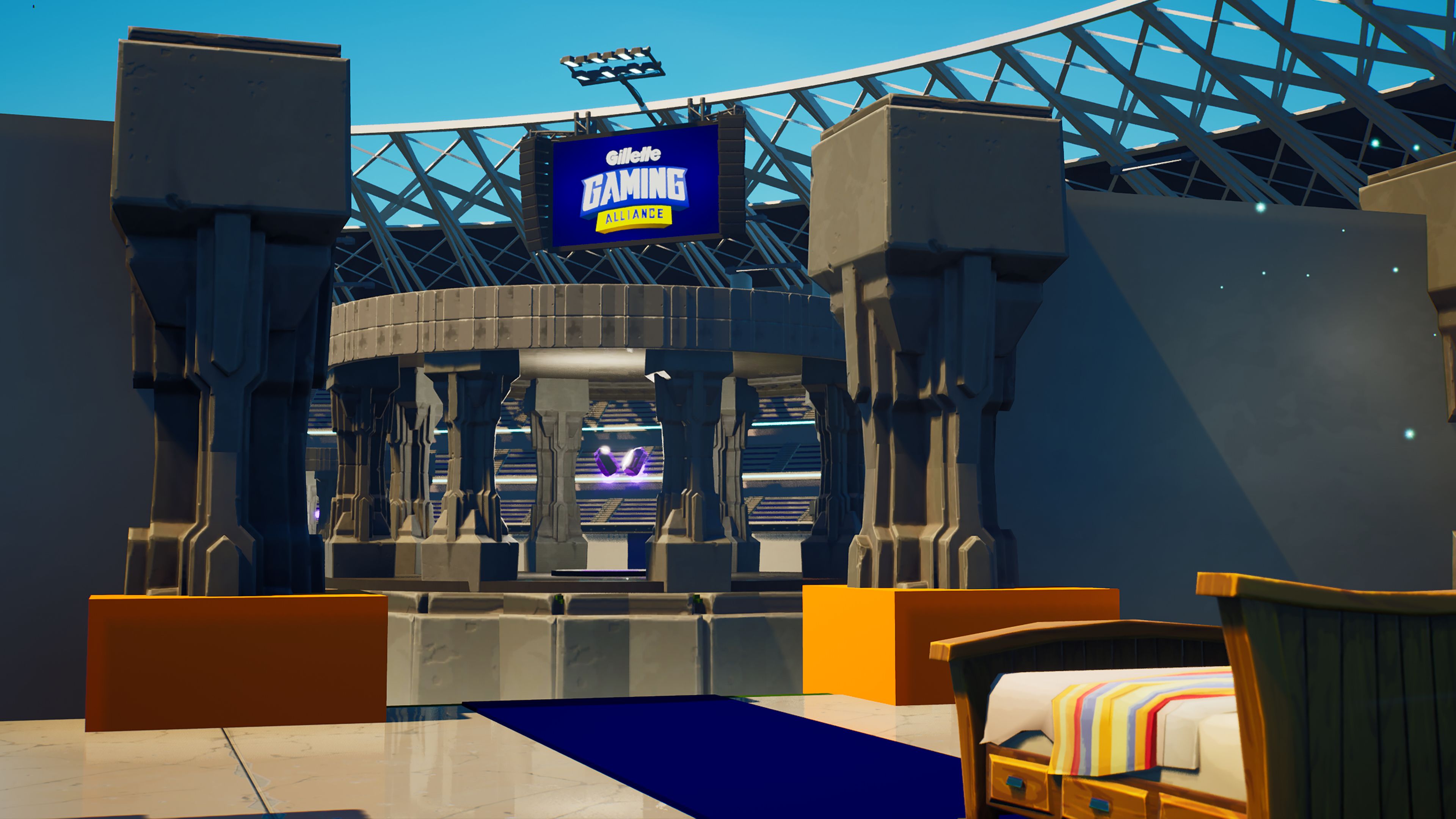 Interior shot of a modern stadium with stone pillars, a Gillette Gaming Alliance sign, and a bed with a striped blanket in the foreground.