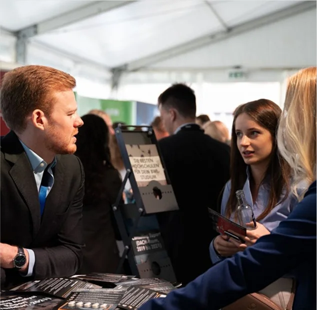 Menschen sprechen auf einer Messe, ein Mann und zwei Frauen im Gespräch in einem Messestand.