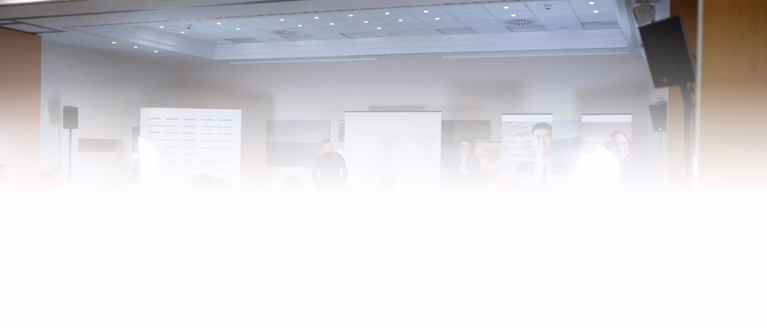 Unscharfe Menschen bei einer Konferenz mit Projektionswand und Bannern im Hintergrund.