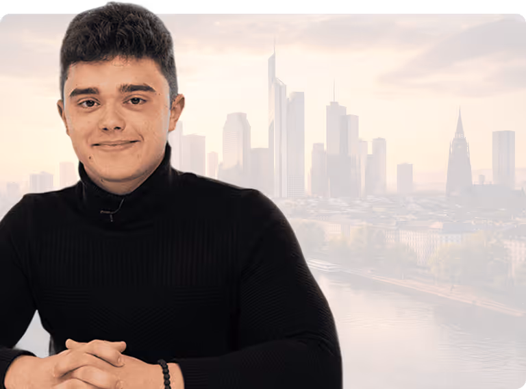 Junger Mann mit schwarzen Haaren und schwarzem Pullover vor einer verschwommenen Stadtansicht.
