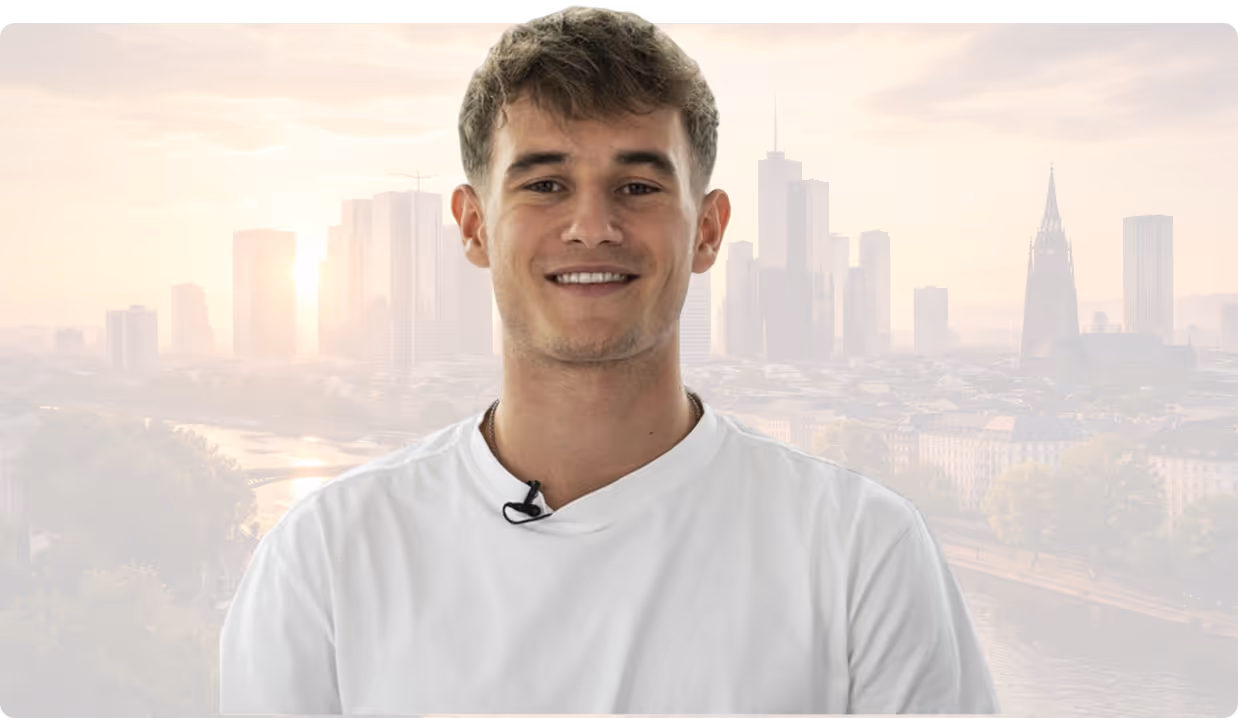 Junger Mann mit weißem T-Shirt lächelt vor verschwommenem Stadtbild mit Hochhäusern bei Sonnenaufgang.