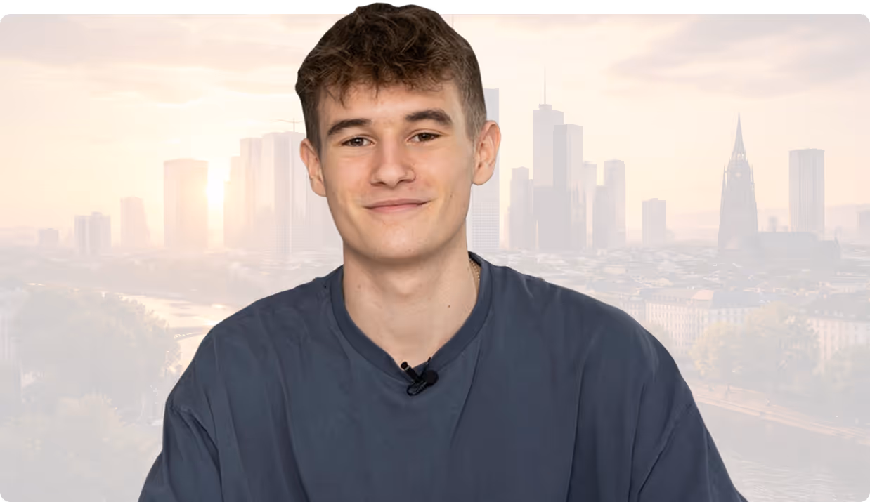 Junger Mann mit dunklem Shirt lächelt vor einer städtischen Skyline im Hintergrund.