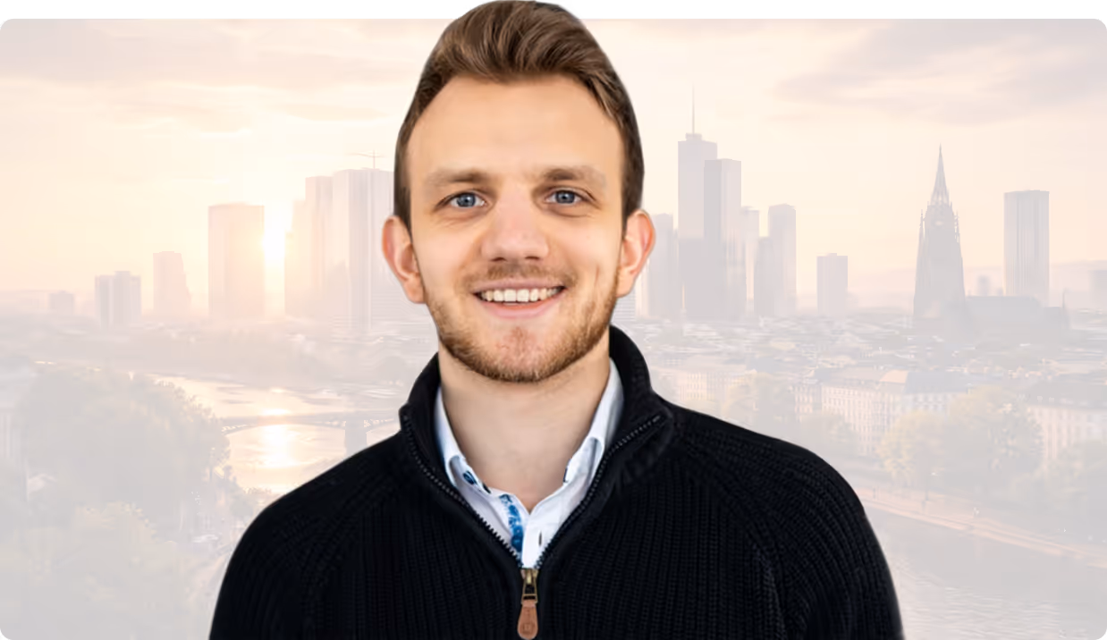 Lächelnder junger Mann mit kurzem braunem Haar und schwarzem Pullover vor einer Stadtsilhouette.