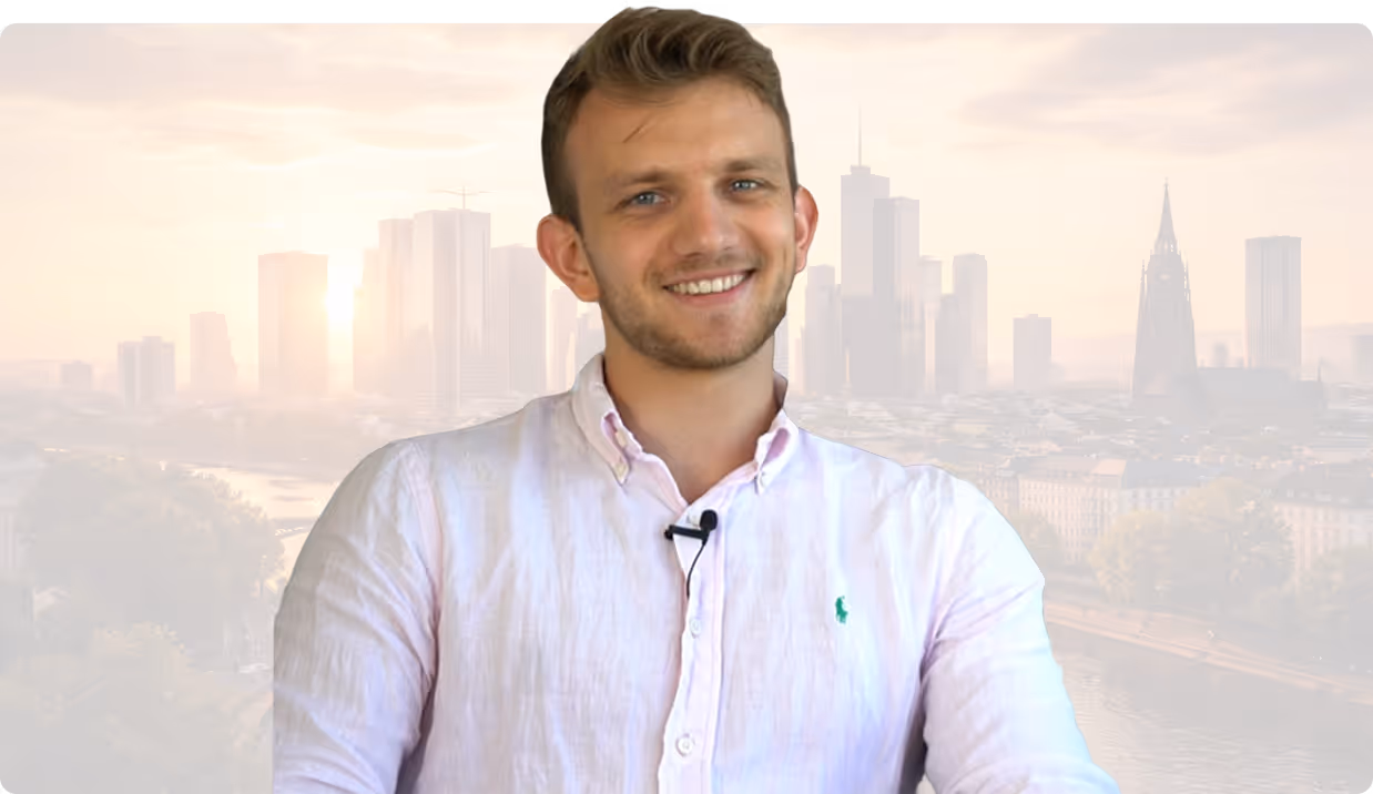 Junger Mann in rosa Hemd lächelnd vor einer Stadt-Skyline im Morgendunst.