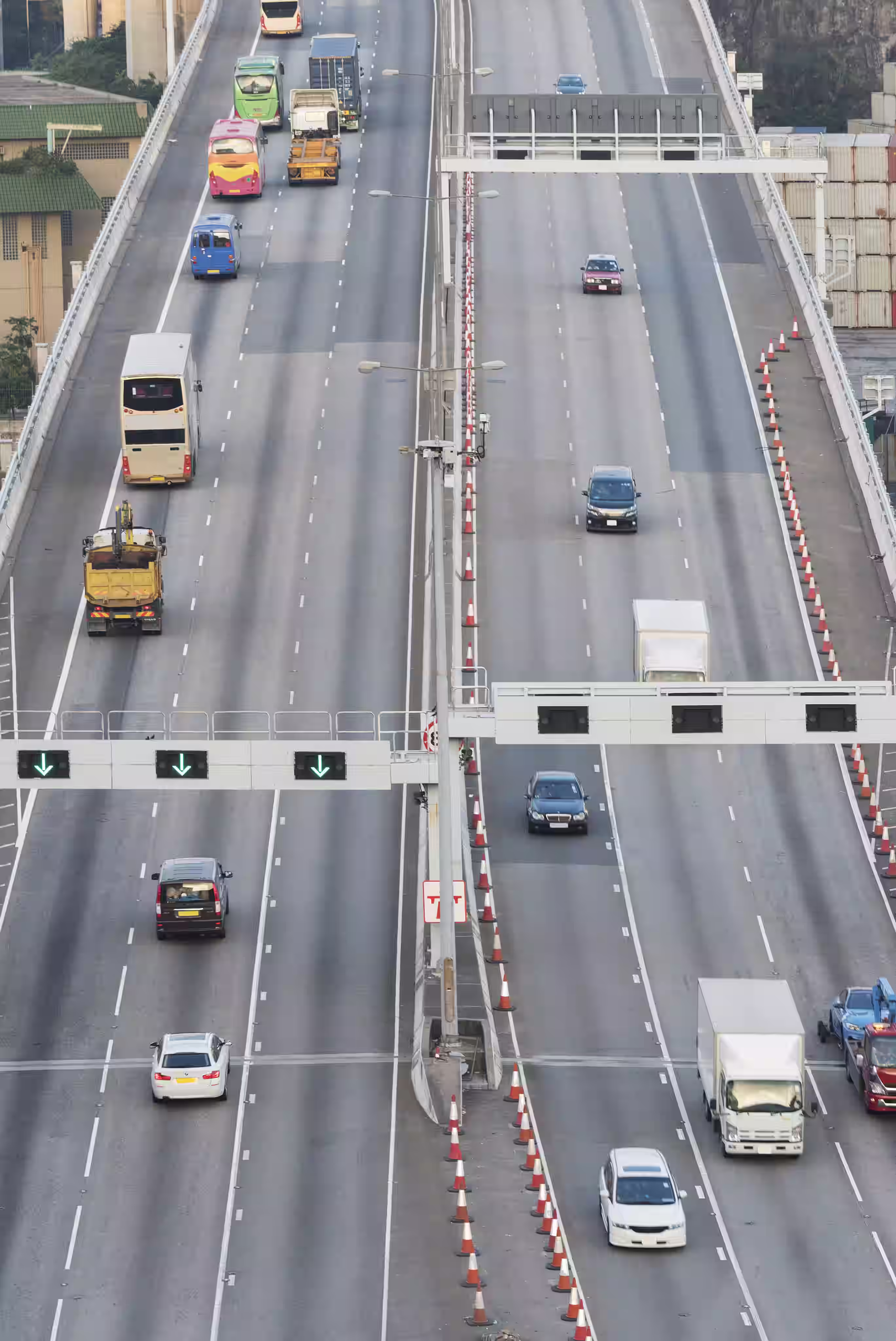 Elevated view of a divided multi-lane highway with various vehicles including cars, buses, and trucks, and traffic cones along the right side.