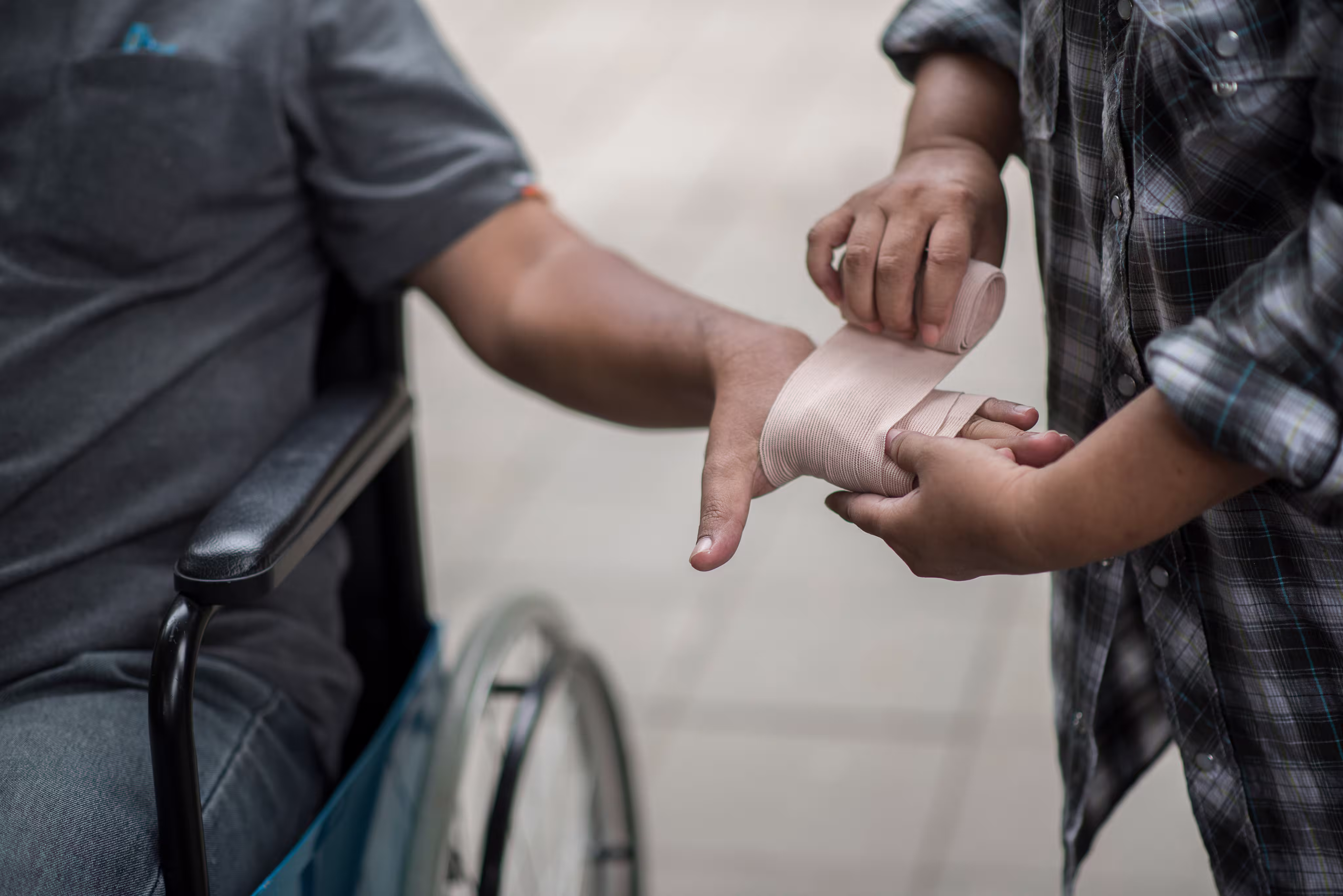 Person wrapping an elastic bandage around the hand of a person in a wheelchair.