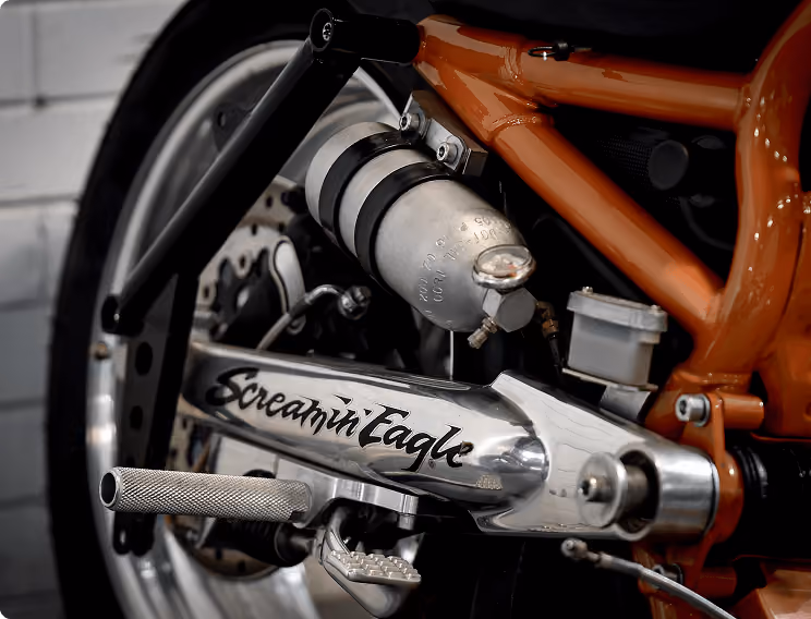 Close-up of a motorcycle's chrome swingarm with 'Screamin Eagle' branding on an orange frame.