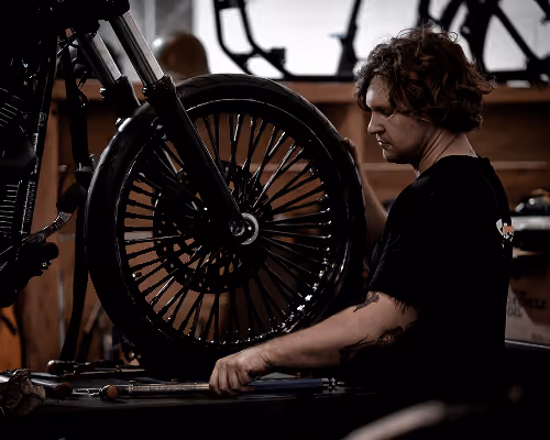 Man working on a motorcycle wheel in a dimly lit garage or workshop.