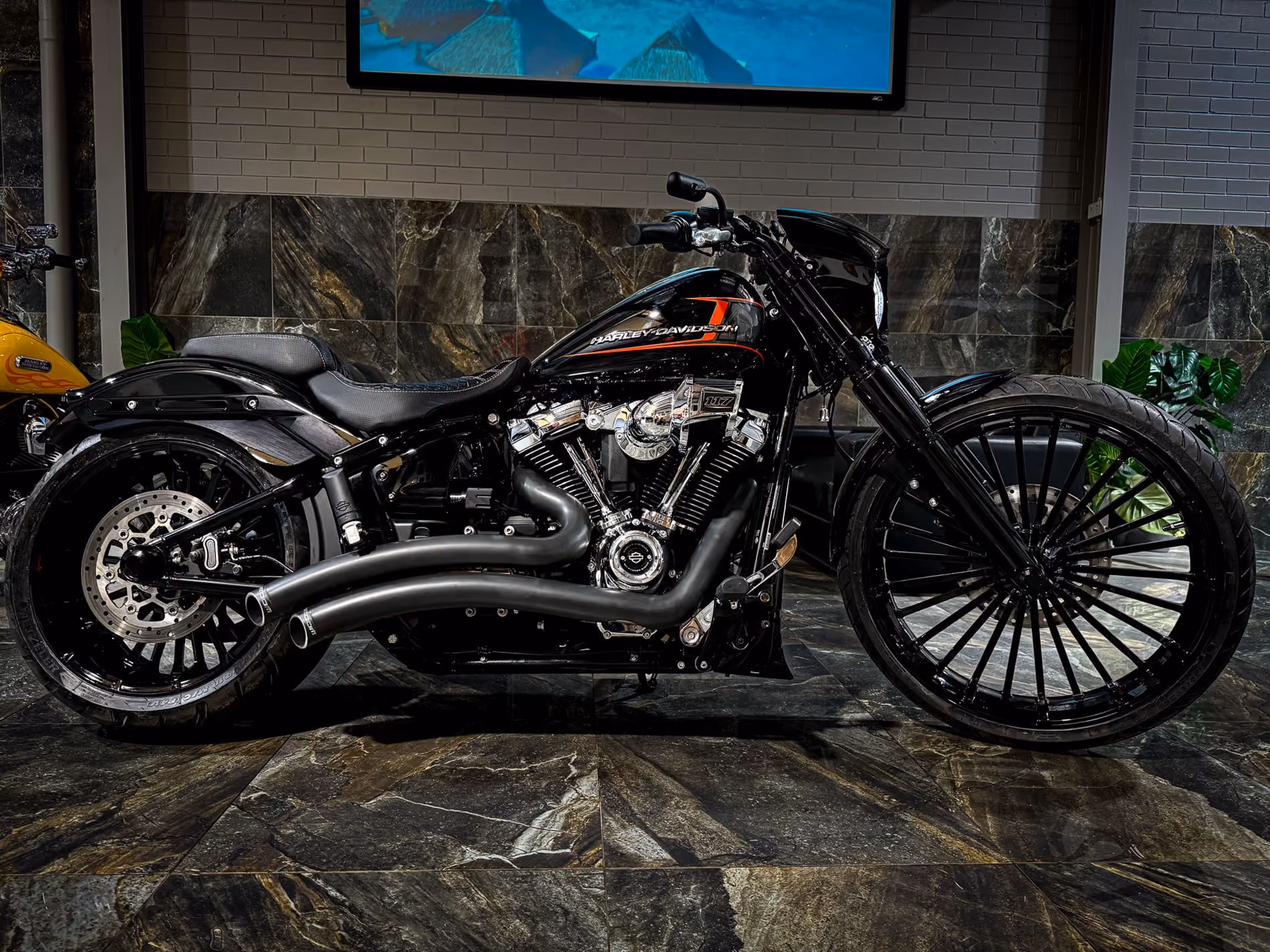 Black Harley-Davidson motorcycle with large front wheel displayed indoors on stone flooring.