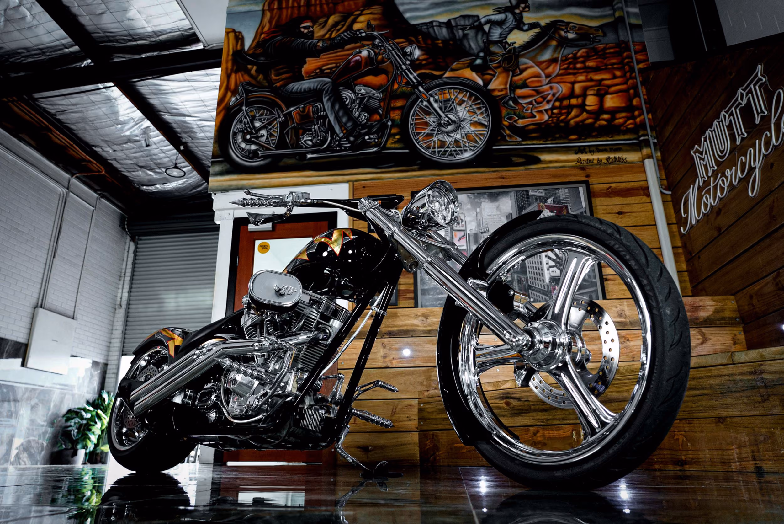 Custom black chopper motorcycle with chrome details displayed in a garage with murals and wood paneling.