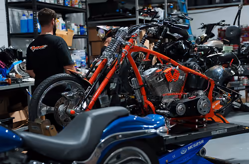 A custom red motorcycle frame without wheels being assembled in a workshop with a mechanic working nearby.