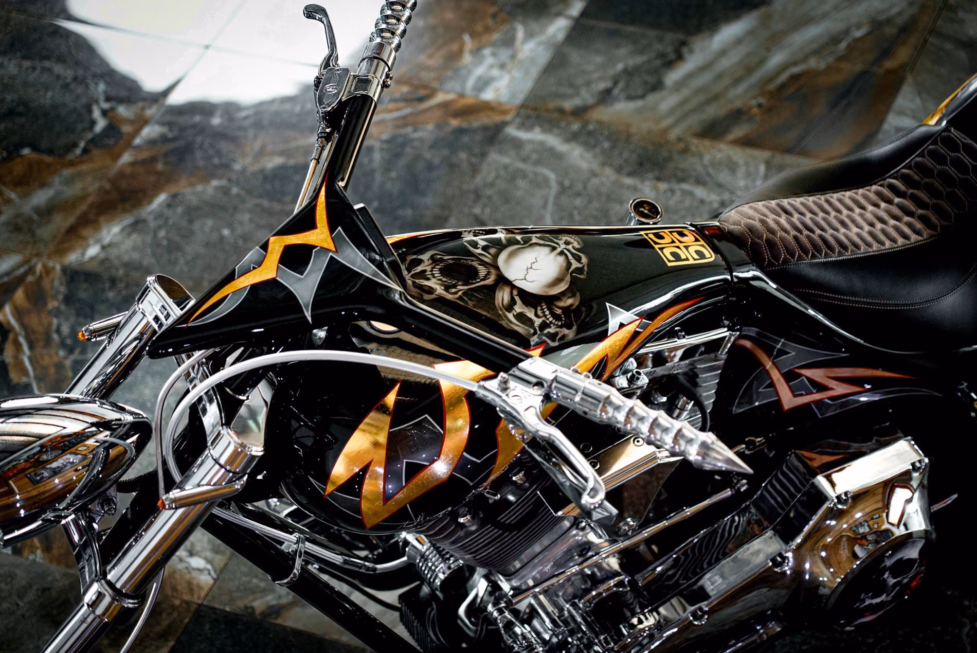 Close-up of a custom black motorcycle with gold and orange flame decals and skull artwork on the fuel tank.