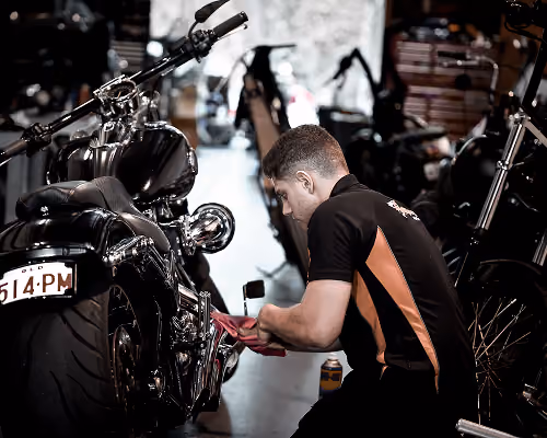 Man cleaning polished black motorcycle inside a garage with other bikes in the background.