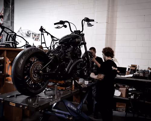 Two people working on a black motorcycle lifted on a service platform in a workshop.