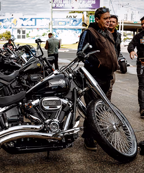 Man standing beside a black Harley-Davidson motorcycle with a large front wheel in an outdoor setting.