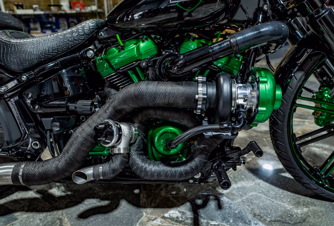 Close-up of a motorcycle engine featuring green parts and black wrapped exhaust pipes.
