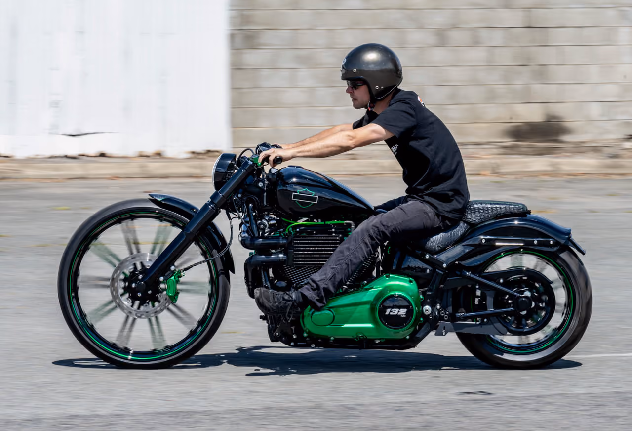 Person wearing black helmet riding a custom black and green motorcycle on a paved surface.