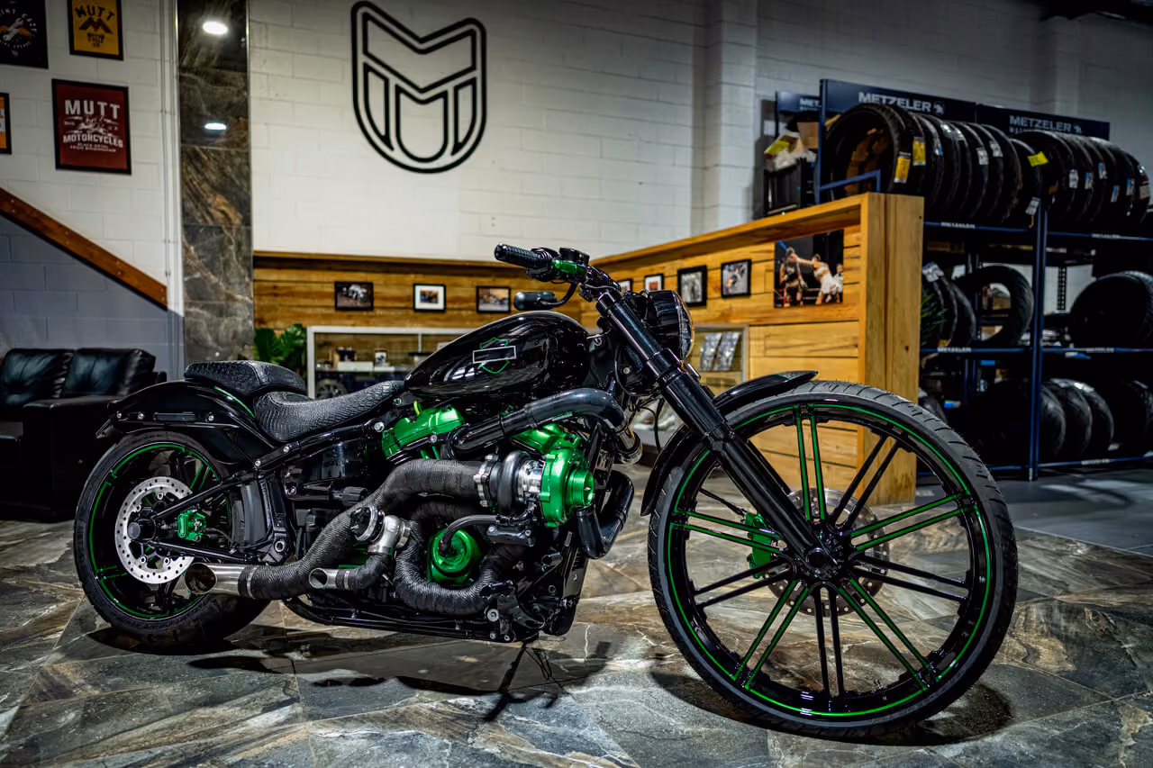 Custom black motorcycle with green engine parts and rims inside a showroom with tire racks.