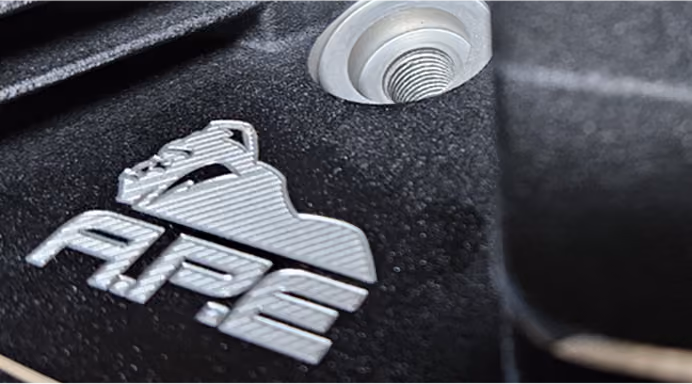 Close-up of a black textured surface with metallic APE logo and a round metal bolt.