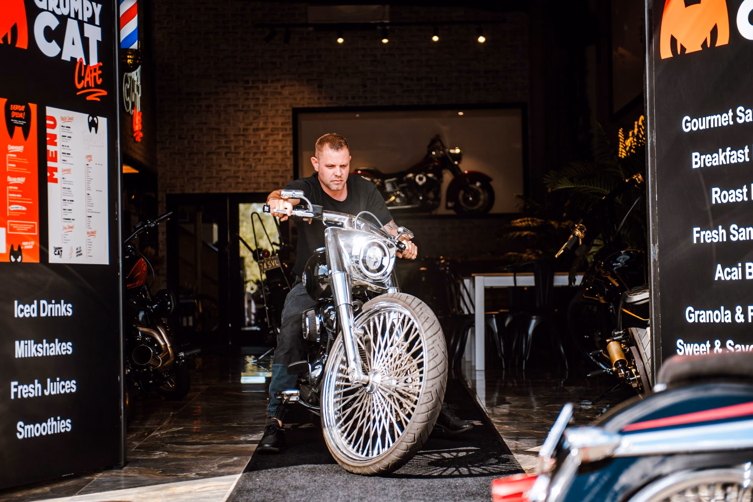 Man riding a large motorcycle indoors between two cafe menu boards at Grumpy Cat Cafe.
