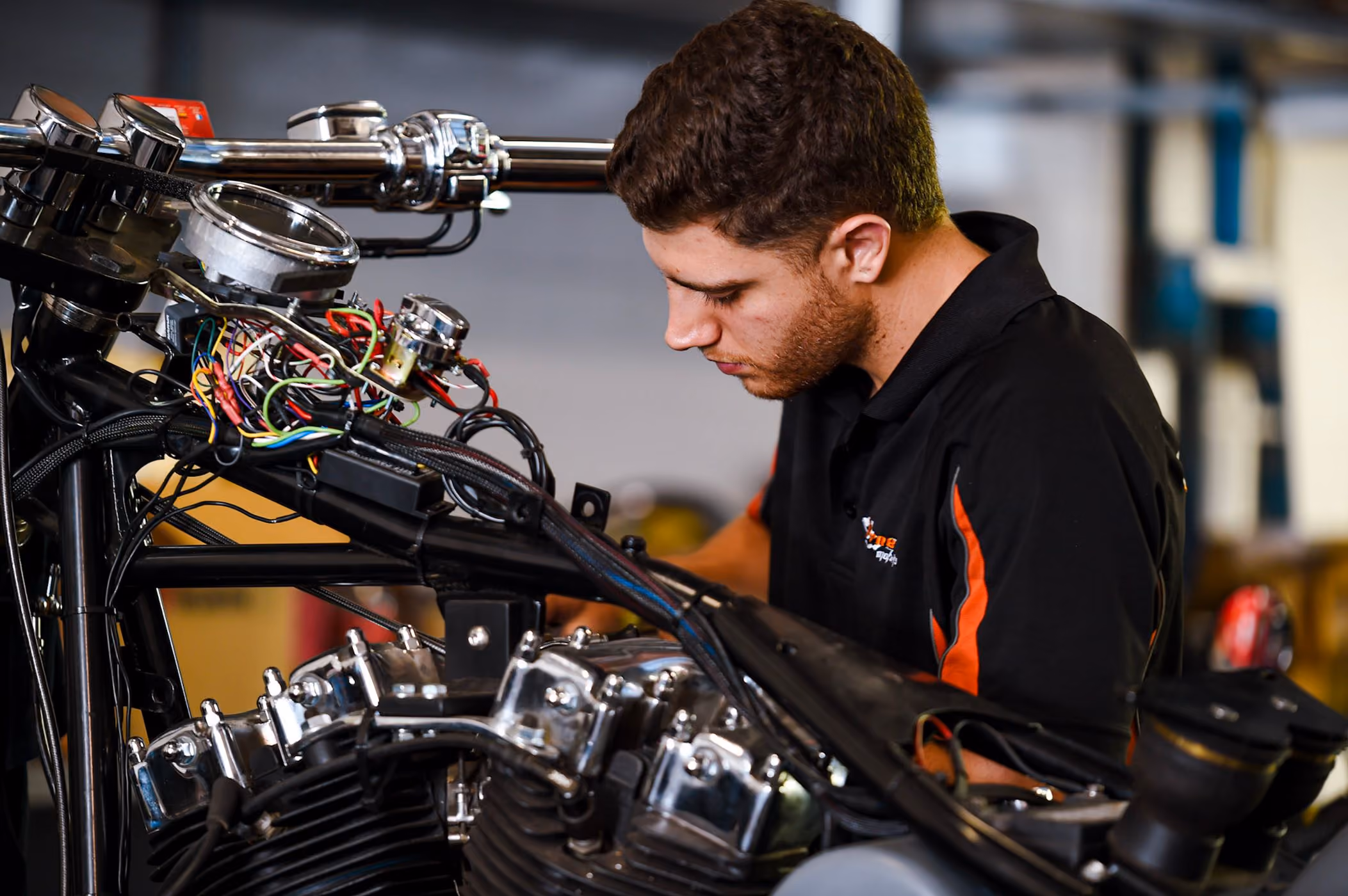 Man in black shirt working on wiring and engine of a motorcycle in a workshop.
