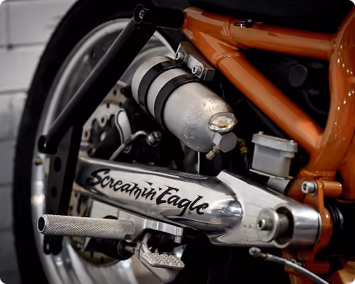 Close-up of a motorcycle's chrome part with Screamin' Eagle logo and orange frame.
