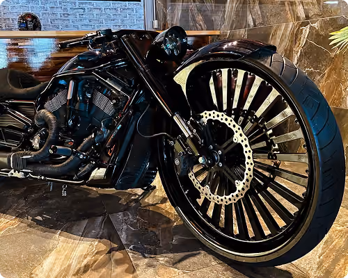 Close-up of a custom black motorcycle focusing on its large front wheel and engine details indoors.