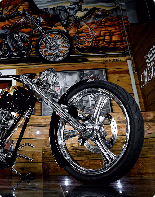 Close-up of a shiny chrome motorcycle wheel with murals of motorcyclists on horseback in the background.