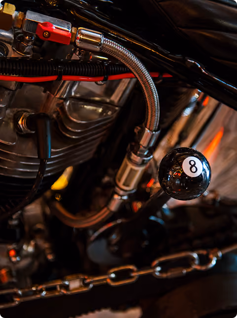 Motorcycle gear shift knob shaped like a black 8-ball on a metallic engine background.