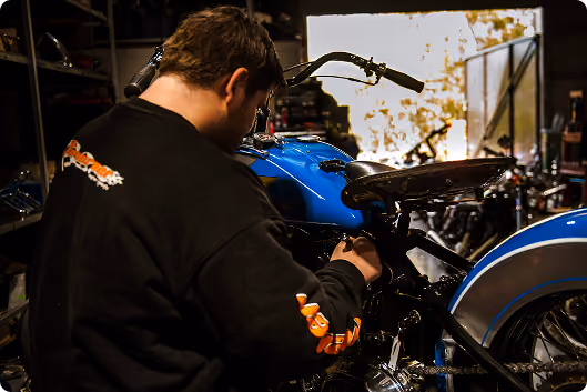 Man working on a blue motorcycle in a dimly lit garage or workshop.