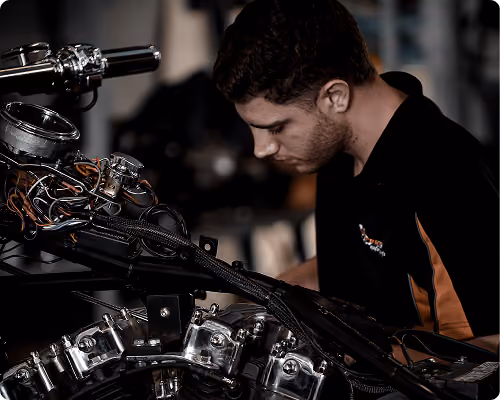 Man focused on repairing a motorcycle engine with visible wiring and chrome parts.