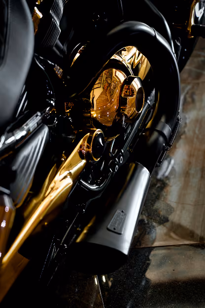 Close-up of a motorcycle engine and exhaust pipe with gold and black details on a reflective floor.