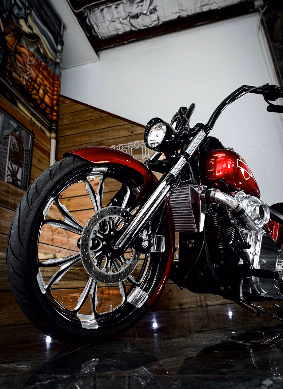 Close-up of a shiny red motorcycle front wheel and headlight in a room with wooden walls.
