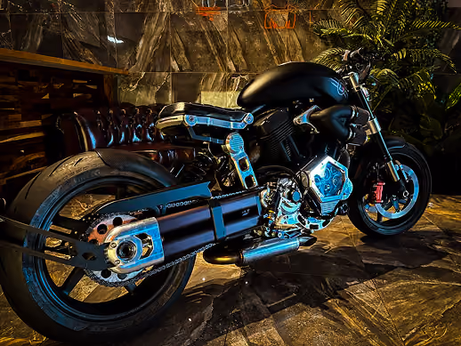 Black custom motorcycle with chrome details parked indoors on a polished stone floor.