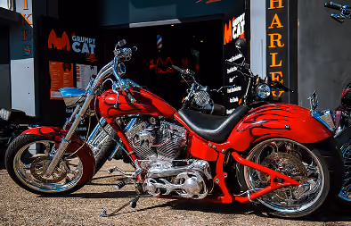 Shiny red custom Harley-Davidson motorcycle parked outside a building with Harley signage.