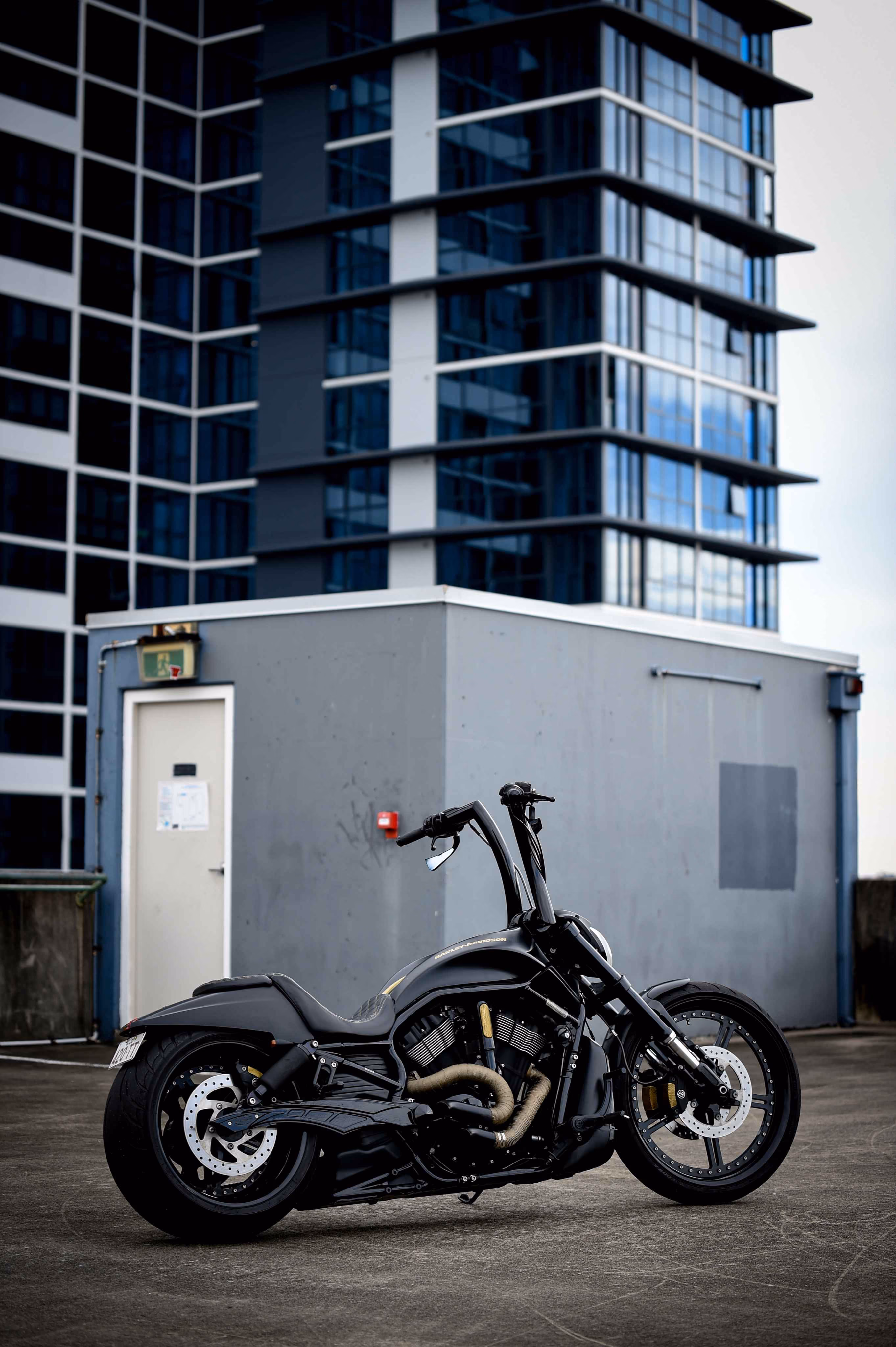 Black Harley-Davidson motorcycle parked on rooftop with modern glass building in background.