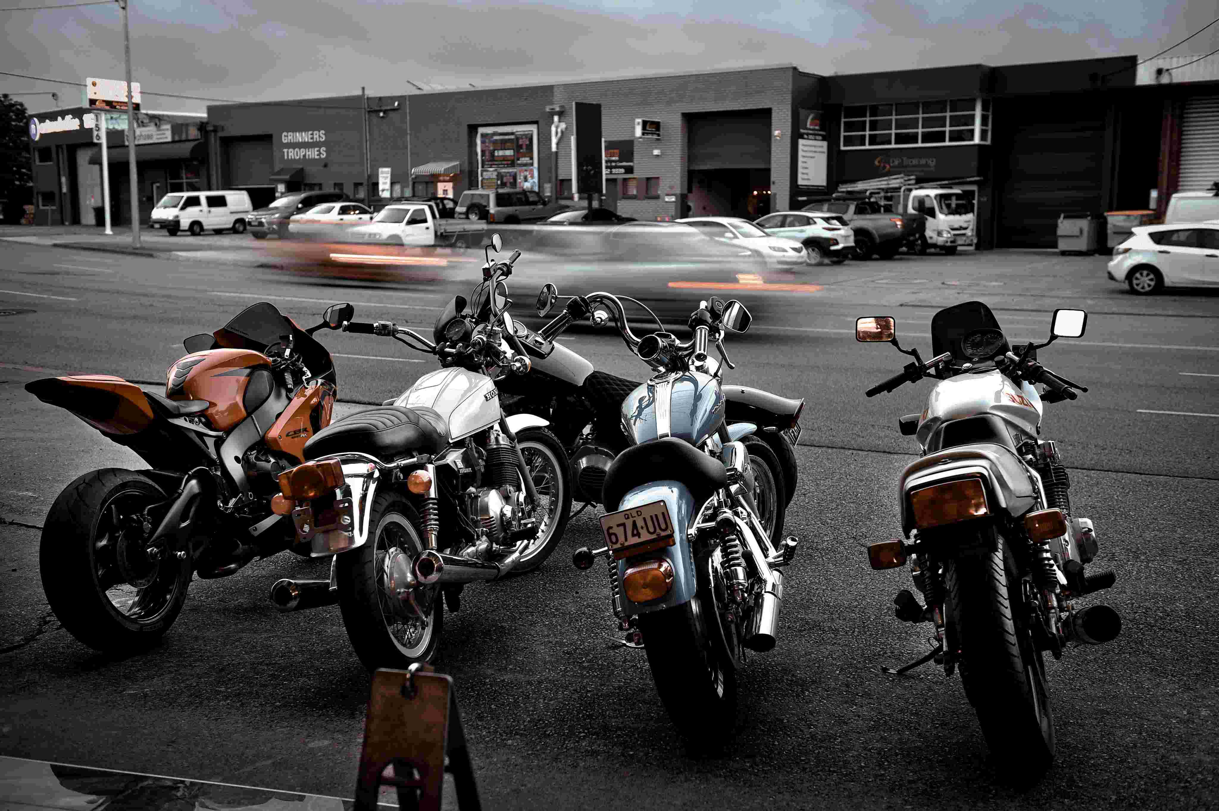 Four motorcycles parked side by side on an urban street with blurred cars passing behind.